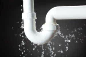 A close-up photo of a broken white pipe spraying water in a house. Burst water pipe in house.