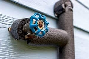 Close-up of a blue valve on a pipe insulated with white foam pipe insulation.