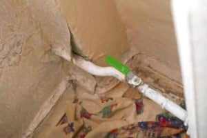 Green shutoff valve on a white pipe, secured with a metal strap. Strap plumbing uses metal straps to secure pipes, especially in areas prone to movement or vibration.