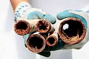 A person wearing gloves holding up multiple corroded and clogged pipes, illustrating the severity of plumbing issues. This image can be used to emphasize the importance of knowing how to unclog a toilet without a plunger as part of a comprehensive guide.