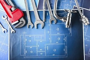 Essential tools and materials for fixing a tap dripping water, including wrenches, a pipe wrench, a faucet, and plumbing hoses, arranged on top of architectural blueprints. This image highlights the necessary equipment for repairing a leaky faucet.