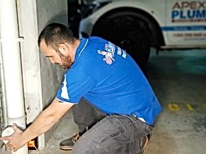 Plumber fixing a burst pipe under house next to white wall.