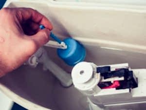 Hand adjusting the float valve inside the tank of a toilet that won't refill, ensuring proper operation.